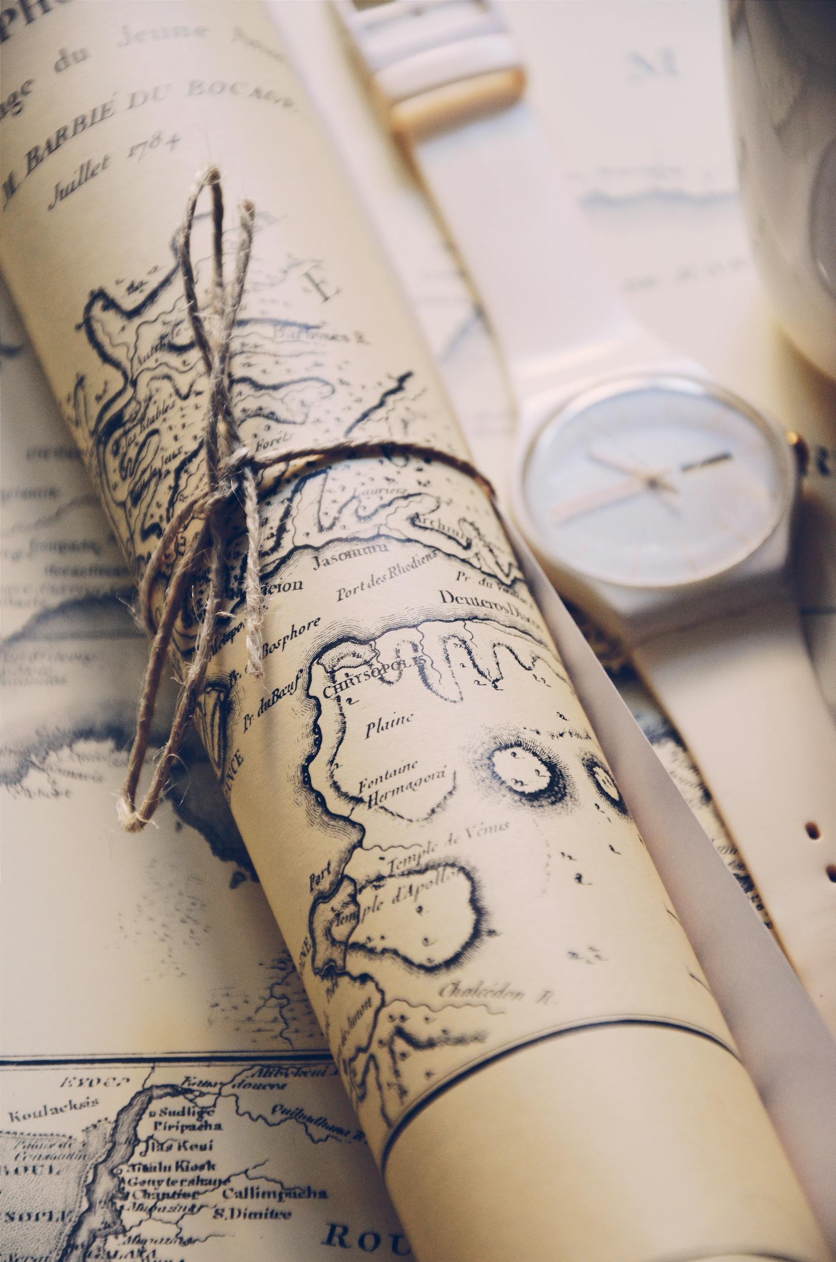 Close-up of a rolled vintage map tied with string, accompanied by a wristwatch.